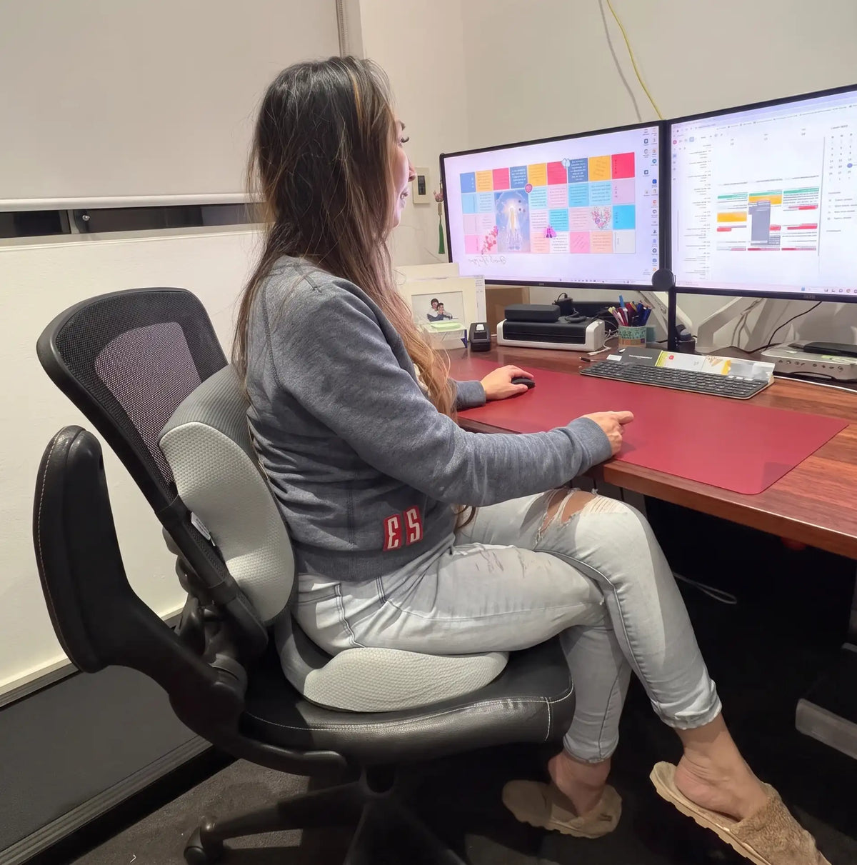 Woman sitting at a two-monitor desk using the ComfortBundle seat cushion and lumbar support